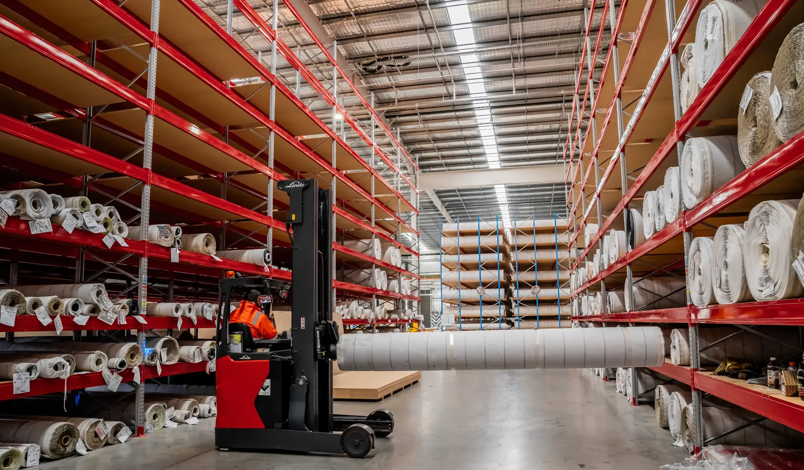 Forklift transporting rolled materials through a warehouse with organised industrial shelving and efficient storage layout.